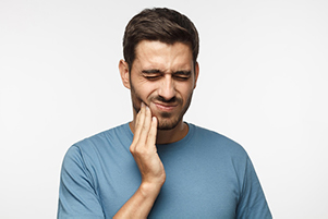 male patient holding his hand up to his lower jaw and grimacing with pain