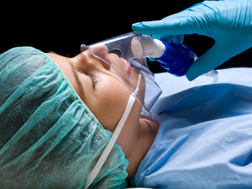 General anesthesia sedation: gloved hand holds breathing mask to sleeping patient's face